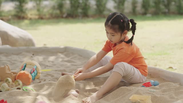 Asian girl children playing sand on the playground in the cafe for kids. Little girl playing in the sand on the playground. Healthy active baby outdoors plays games concept.
