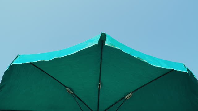 Green beach umbrella. Blue sky in the background. View from below. Relaxing context. Summer holidays by the sea. General contest and location