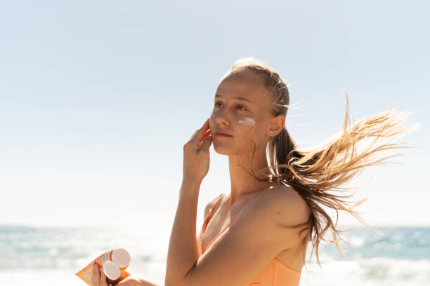 istock Young woman applying sunscreen on her face while at the beach 2148229640