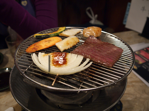 Cooking japanese wagyu marbled beef and vegetable slices on round yakiniku grill