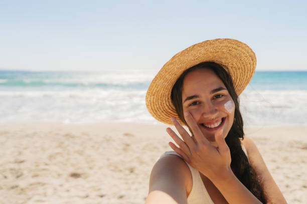 istock Young woman applying sunscreen on her face while at the beach 2148230676