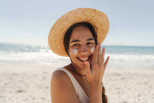 istock Young woman applying sunscreen on her face while at the beach 2148230787