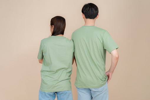 An image of a male and female fashion model standing in green t-shirt and jeans standing in studio on beige background, trendy clothing style, copy space
