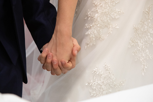 a tender moment as newlyweds hold hands, their wedding attire and rings symbolizing a lifelong union