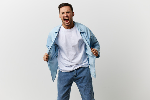 Angry irritated tanned handsome man in blue basic t-shirt scream growl at camera posing isolated on white studio background. Copy space Banner Mockup. People emotions Abusive relationships concept