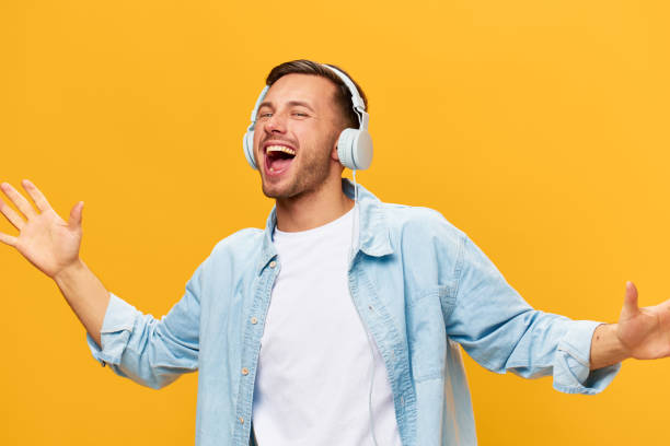 istock Singing overjoyed tanned handsome man in blue basic t-shirt headphones spread hands dance posing isolated on orange yellow studio background. Copy space Banner Mockup. Time to relax concept 2148231670