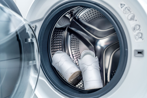 A pair of white sneakers in the washing machine. Footwear hygiene.