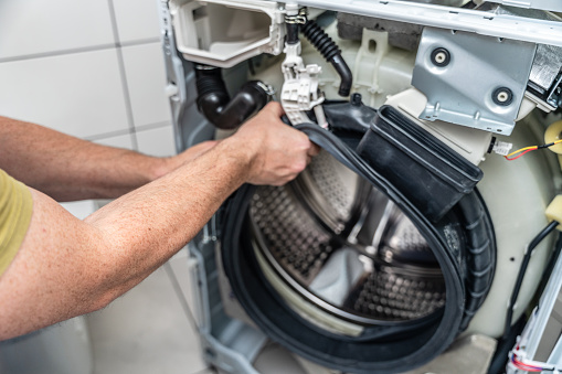 A repairman removes damaged gasket of the front lid door of washing machine