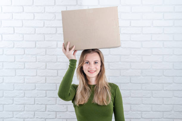 istock Attractive woman holding parcel box on head. Delivering a parcel 2148233139