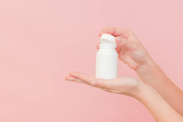 istock White bottle plastic tube in woman's hands on pink background. Packaging for pills, capsules or supplements. Cosmetics 2148233156