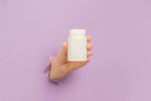istock View on white bottle plastic tube in hands on lilac background. Packaging for pills, capsules, supplements. Cosmetics 2148233167