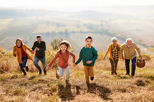 Carefree multi-generation family holding hands and having fun while running during autumn day on a hill. Focus is on kids. Copy space.