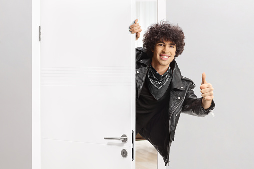 Guy in a black leather jacket behind a door gesturing thumbs up and smiling