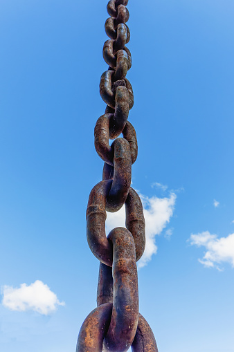 A thick iron chain to divert rainwater against a blue sky background close-up