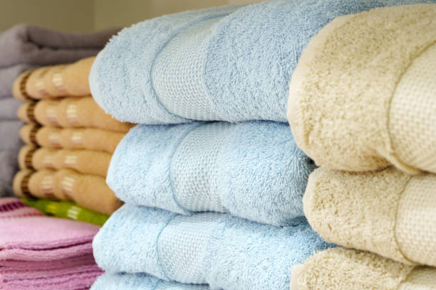 Neatly folded white towels with brown striped details are stacked on a shelf. In the background, a contrasting stack of red fabric adds a pop of color to the scene, highlighting the organization and cleanliness of a retail stores home goods section.