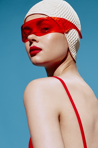 A fashionable young red-lipped female swimmer in a hat and trendy glasses looks over her shoulder. High quality photo