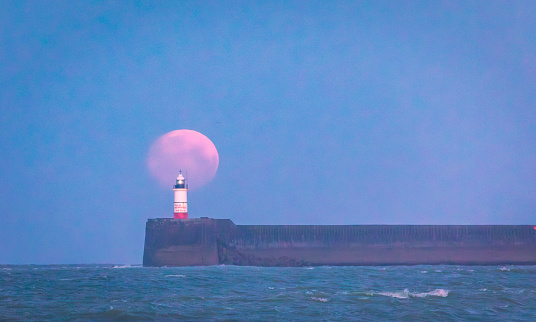 March full moon setting behind Newhaven lighthouse from Seaford beach on the east Sussex coast south east England UK