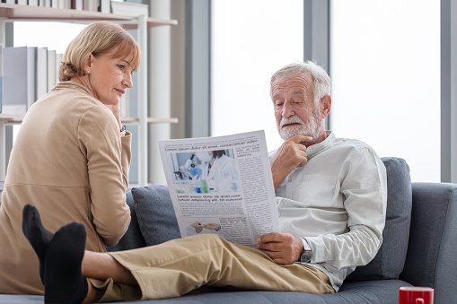 Senior couple spending time together in the living room, Retired man and woman reading newspaper, Happy family concepts