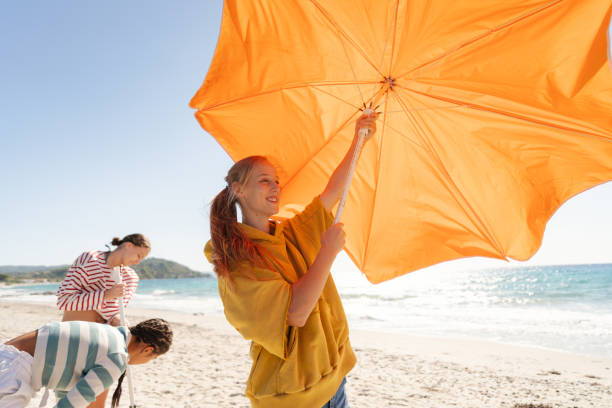 Photo of a couple of female friends setting up a parasol to protect themselves from a summer sun on the local beach