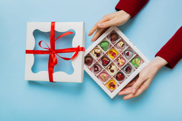 female hands with delicious candies in box on color background - chocolate box human hand giving ストックフォトと画像