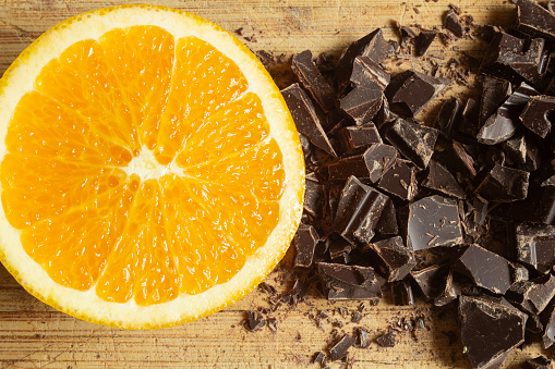 A freshly cut orange lie next to the deep, dark allure of chocolate chunks. The rustic wooden surface beneath them serves as a natural stage, highlighting the interplay of textures and colors.