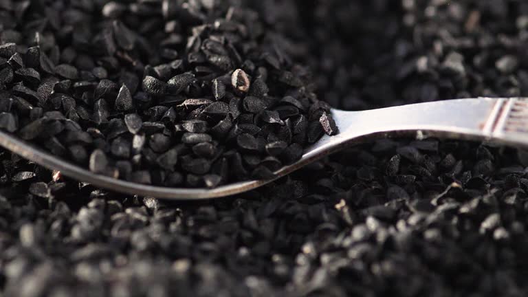 macro black cumin seeds falling on a spoon. slow motion. Asian food seasonings. harvest of black cumin seeds. eating black cumin seeds