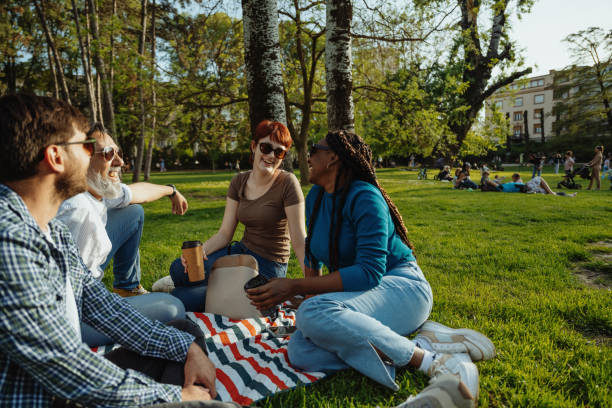 Group of diverse friends outdoors on picnic talking and drinking coffee to go