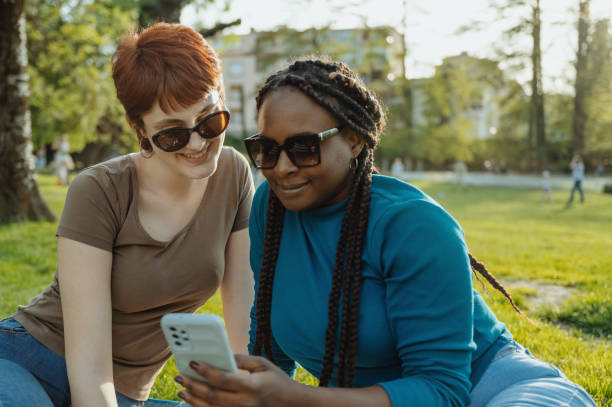 istock Two multi ethnic female friends outdoors on picnic using smart phone on sunny day 2148239941