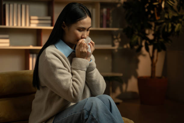 istock Young Asian Woman Blowing Her Nose in a Cozy Home Setting During Evening 2148240616
