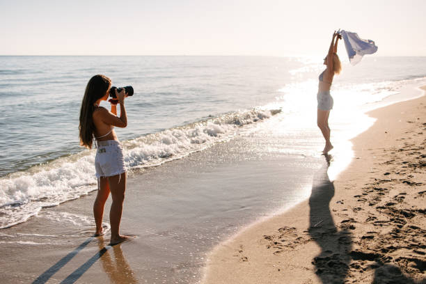 Female photographer taking photos of a young woman by the sea