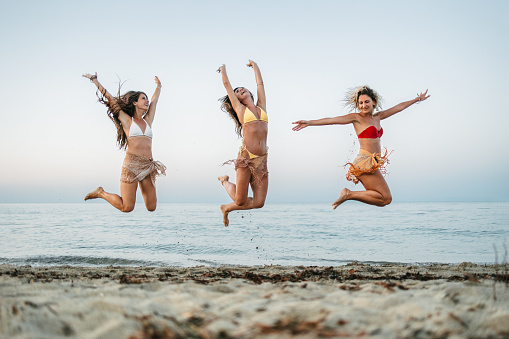 Group of young female friends jumping by the sea at sunset