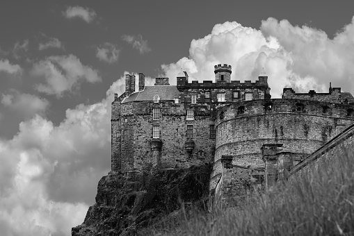Edinburgh - United Kingdom. May 20, 2023: The formidable walls of Edinburgh Castle loom overhead, with cumulus clouds accentuating its commanding presence in this black and white photo