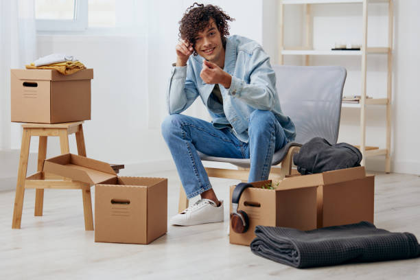 istock A young man sitting on a chair unpacking with box in hand moving interior 2148241541