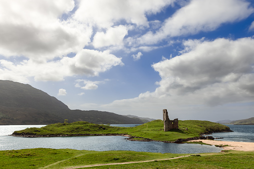 Dornoch - United Kingdom. May 24, 2023: An ancient Ardvreck Castle ruin stands on a lush green islet under a dynamic sky, by the tranquil waters of Loch Assynt