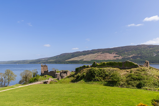 Drumnadrochit - United Kingdom. May 25, 2023: Overlooking the expansive waters of Loch Ness, Urquhart Castle ruins stand resolute under the Scottish sun, surrounded by lush greenery and the gentle slopes of the Highlands