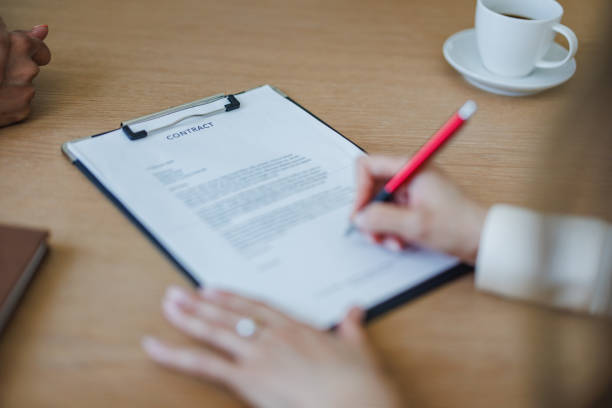 Close-up view of a businesswoman's hands as she signs a contract, with a cup of coffee nearby, symbolizing agreement and business dealings.