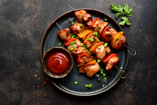 Grilled chicken kebab on a plate over dark metal tray. Top view with copy space.