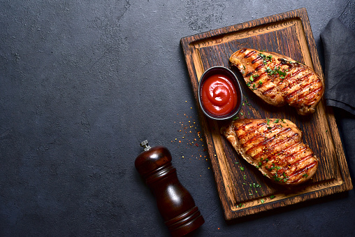 Grilled spicy chicken breasts on a wooden cutting board. Top view with copy space.