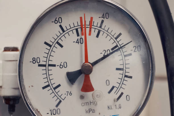 Close-up photograph of an industrial pressure gauge mounted on metal pipe, illuminated by intense orange flames dancing in the dark background, creating stark contrast and dramatic lighting.