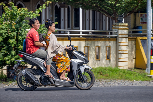 Kuala, North Sumatra, Indonesia - January 25th 2024: Two women with a kid on a motorcycle in the street in a small Indonesian village