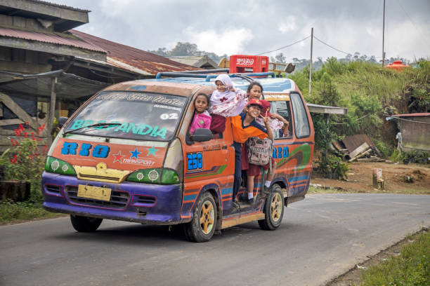 Kuala, North Sumatra, Indonesia - January 25th 2024: Small bus with happy schoolchildren on the road on a rainy day