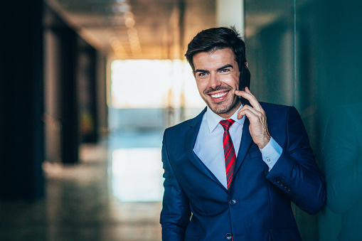 Young smiling businessman using smart phone. Cheerful businessman making phone call.