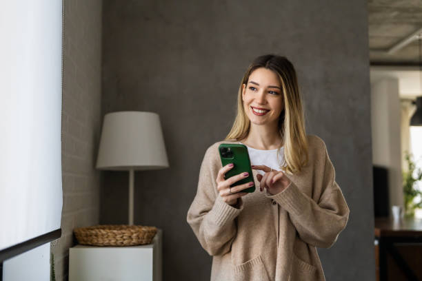 istock Young woman wearing sweater using smartphone at home, communication and social network concept, 2148246981