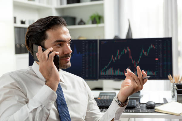 istock Trader calling to consultant or partner with two stock exchange screen. Surmise. 2148247148