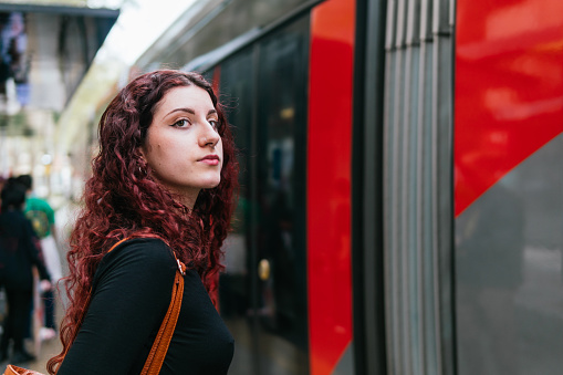 Young redhead woman with piercings on her face waits to board the urban transport car
