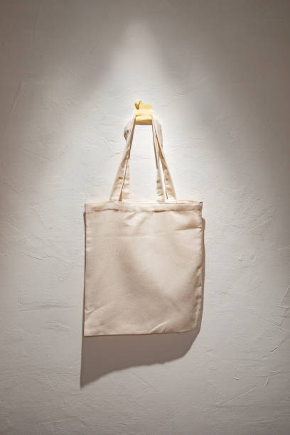istock Simple Canvas Tote Bag Hanging on a White Textured Wall in Soft Lighting 2148249741