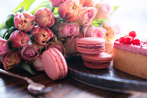 Beautiful pink bouquet of flowers with sweet delicacies. Sweet pastries with pink roses and tulips on a wooden table. Background for mother's day and weddings. Close-up.