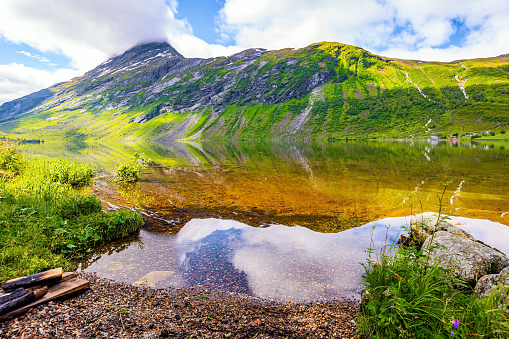 Summer in Scandinavia. The water reflects lush clouds, blue skies and forested shores. Eidsvatnet - majestic lake in Norway. Deep lake with clean transparent water. Green World.