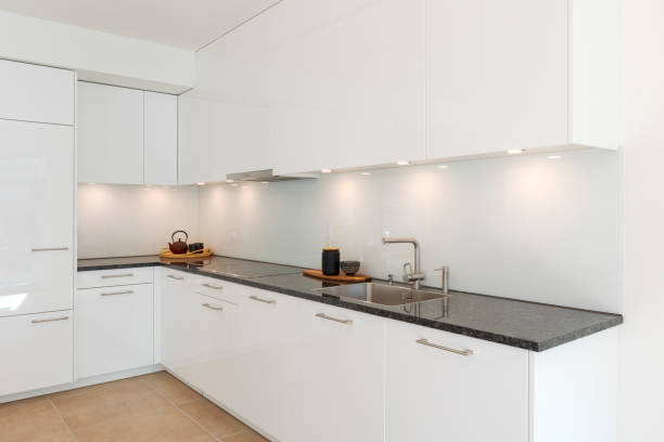 istock Glossy white minimalist modern kitchen with a black marble countertop. Spotlights illuminate the countertop, above which are two trays, one with a teapot and one with a vase 2148253282