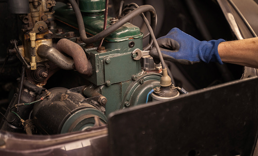 Detail of repairman checking engine of old vehicle in garage